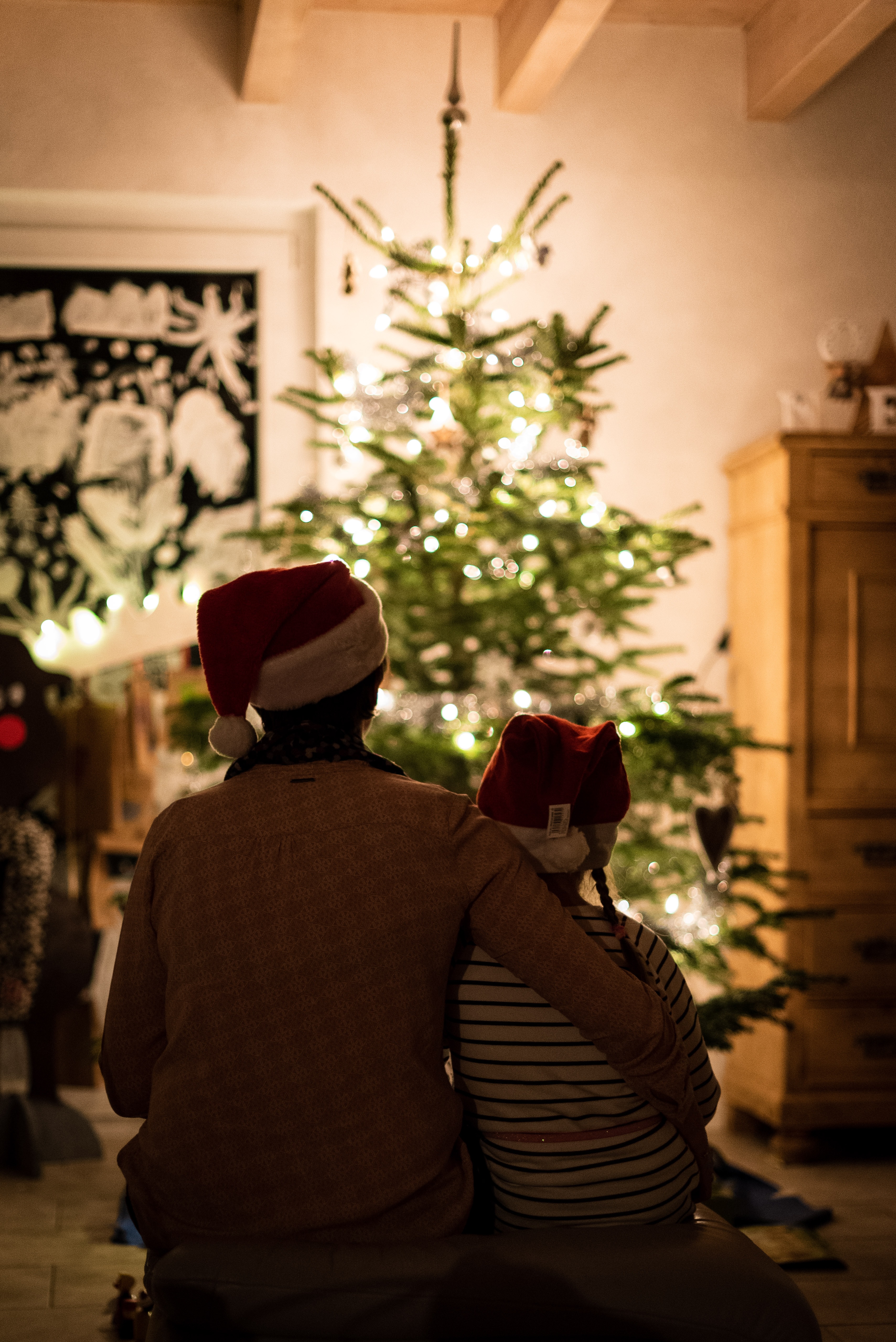 A parent and child sat in front of a Christmas Tree