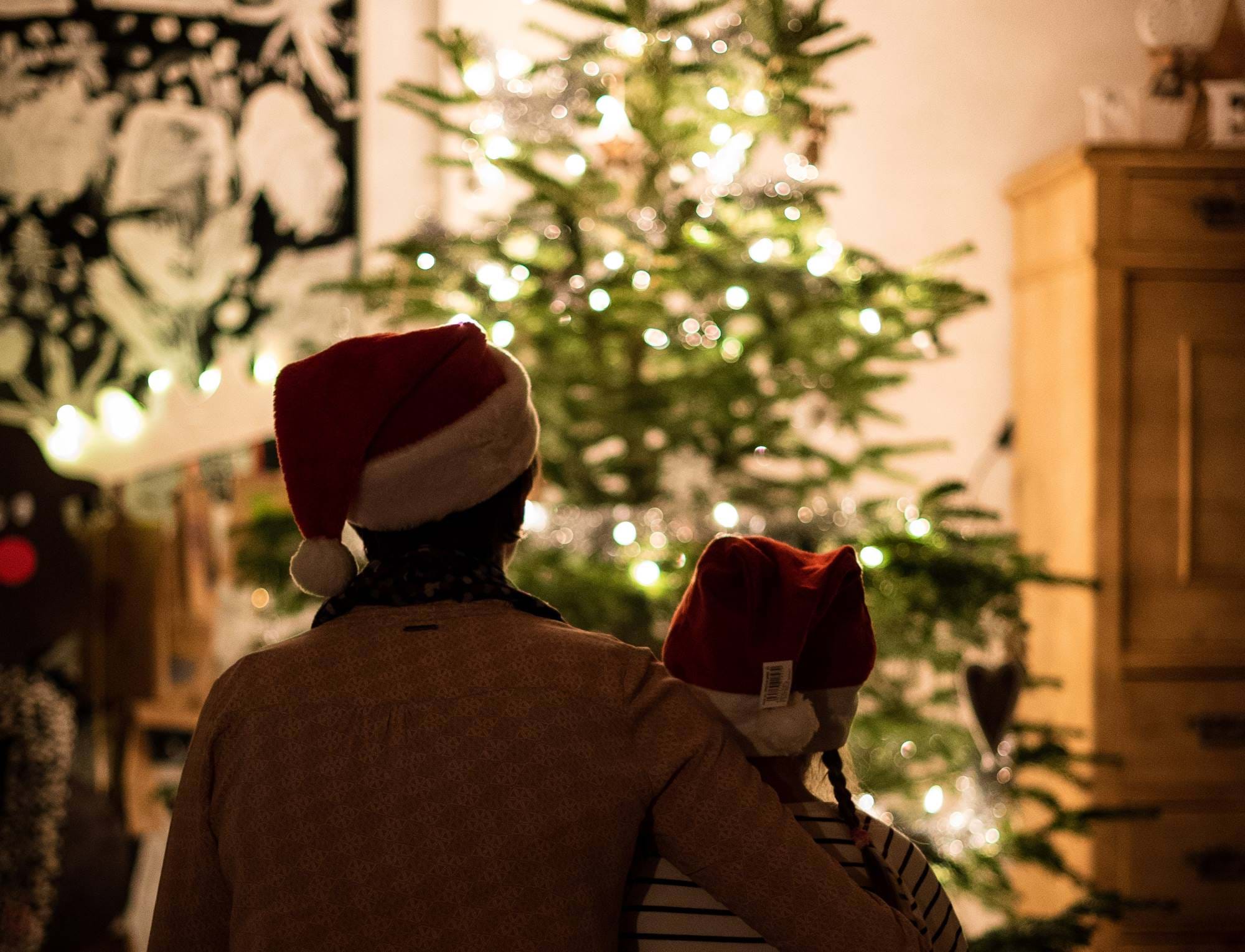 A parent and child sat in front of a Christmas Tree