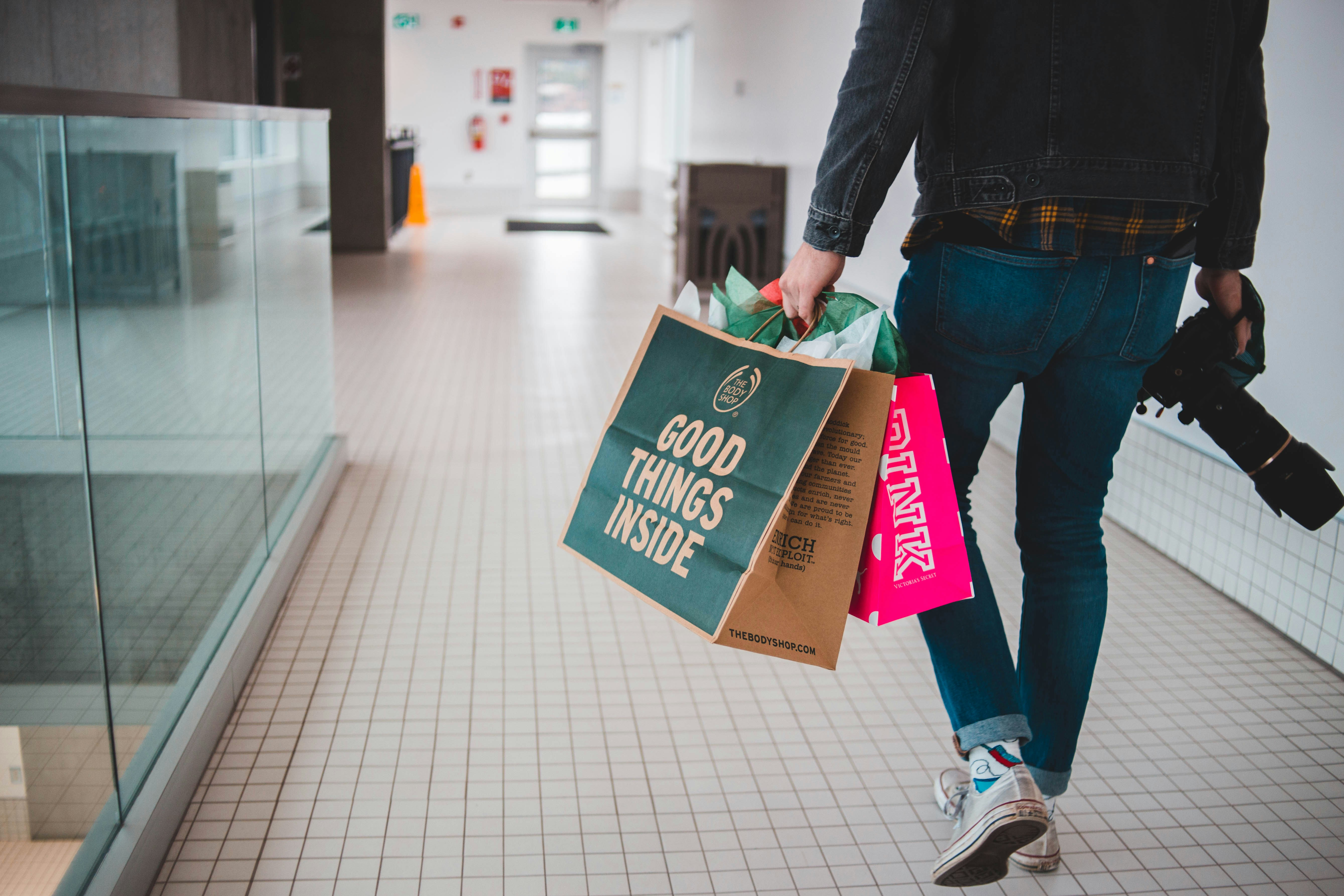 A man walking with a camera and shopping bags in his hands